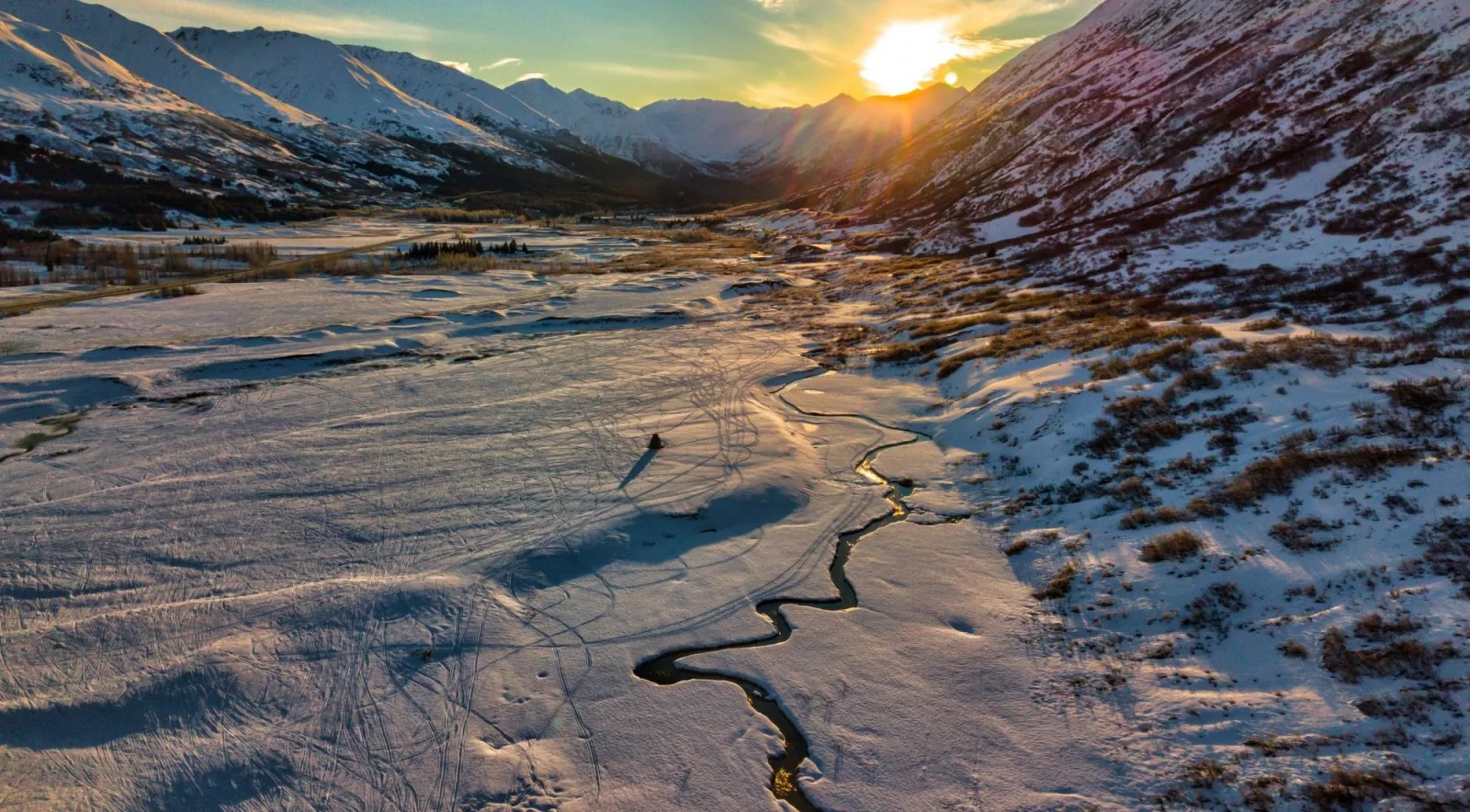 Low sun over a snowy mountain valley with a frozen stream winding through it