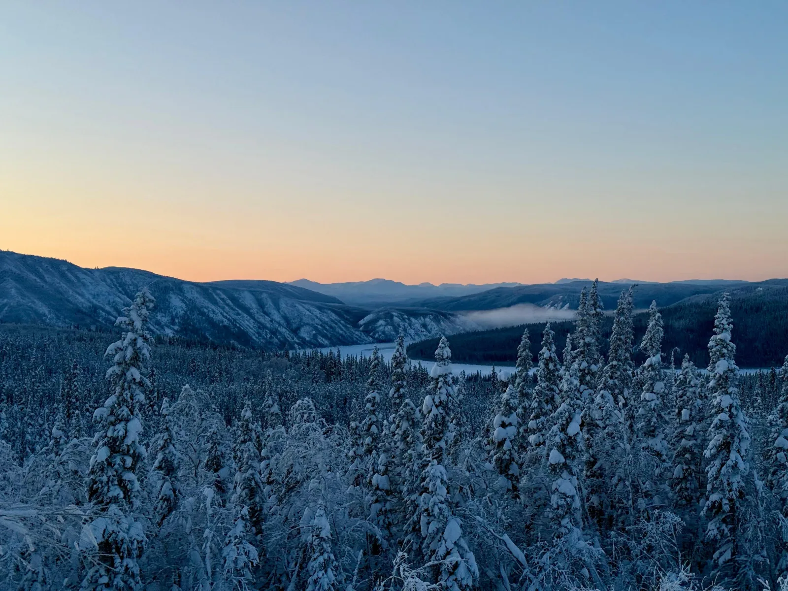 Snow-covered boreal forest and the frozen Yukon River valley under an orange winter sunset