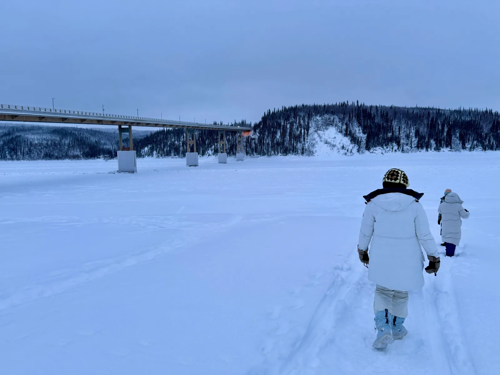 Two guests walking on the frozen Yukon River toward the Dalton Highway bridge at milepost 56