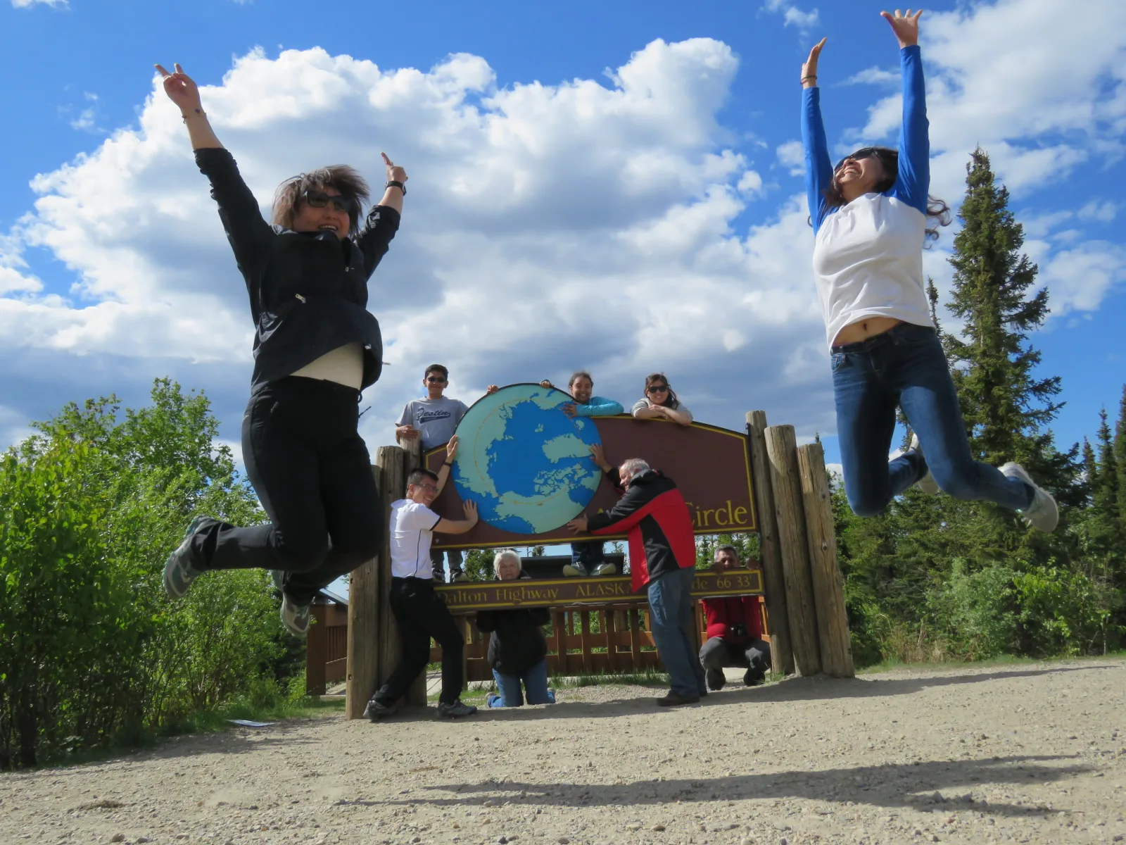 Tour group posing and jumping in front of the Arctic Circle sign under a summer sky