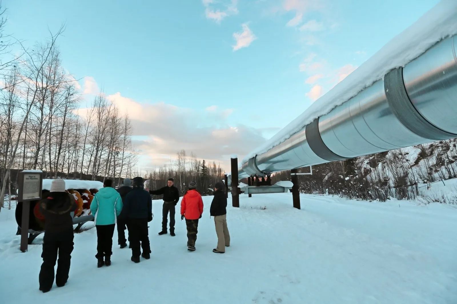 Guide explaining the elevated Trans-Alaska Pipeline to a small group in winter clothing at the viewing area