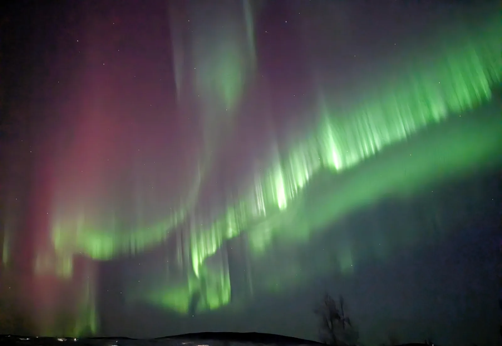 Green and pink aurora curtains filling the night sky above a dark ridge on the Dalton Highway