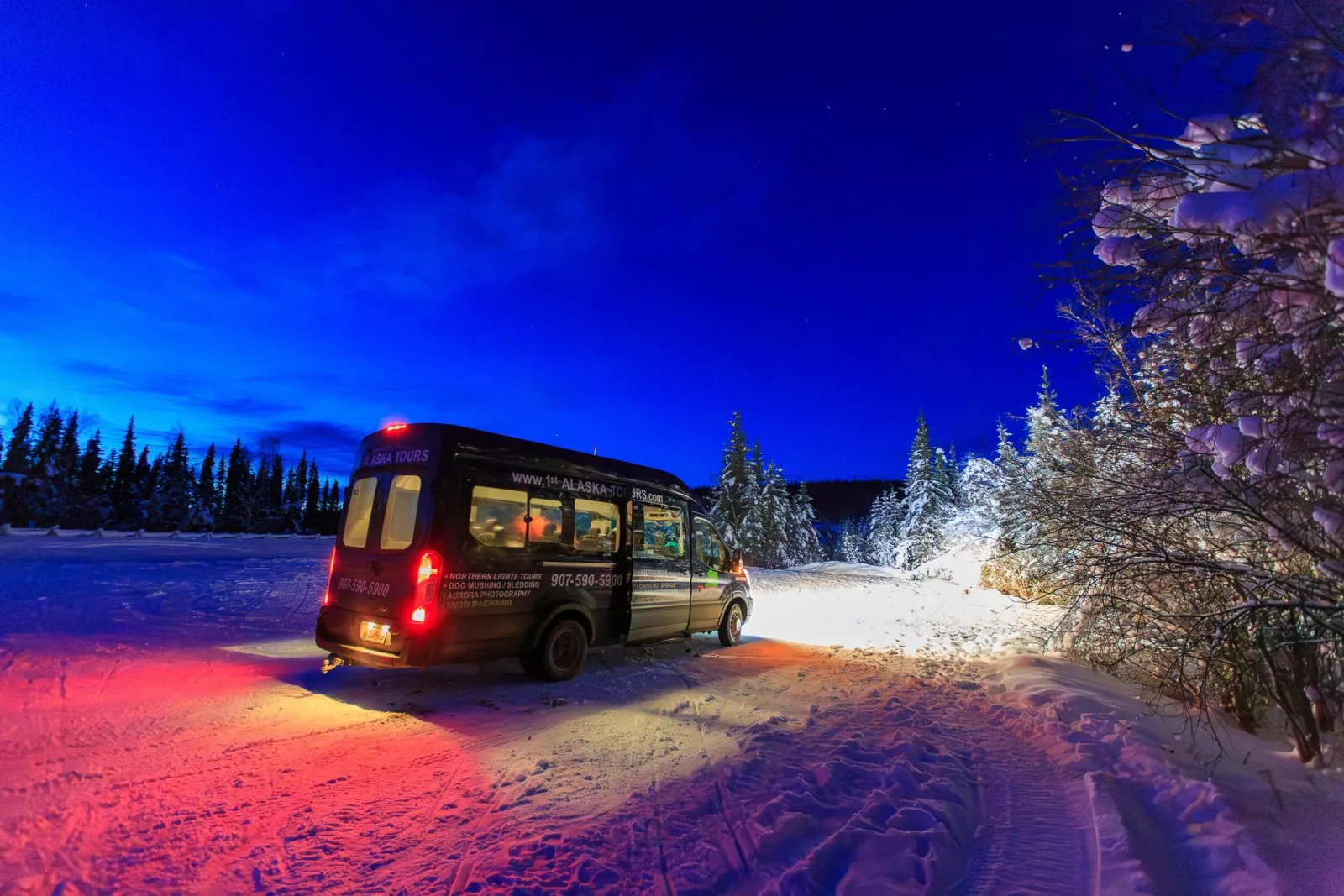 1st Alaska Tours passenger van parked on a snowy pullout at dusk with snow-laden spruce trees