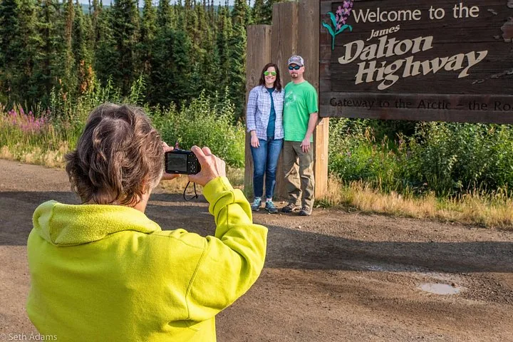 Guest photographing a couple at the Welcome to the James Dalton Highway sign