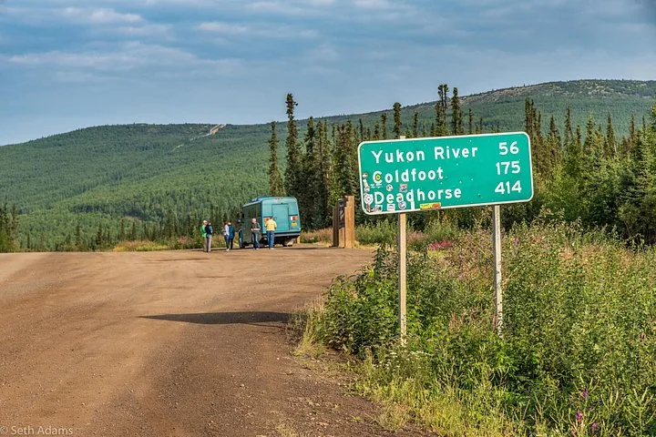 Northern Alaska Tour Company coach parked at the start of the Dalton Highway beside the Yukon River 56, Coldfoot 175, Deadhorse 414 mileage sign