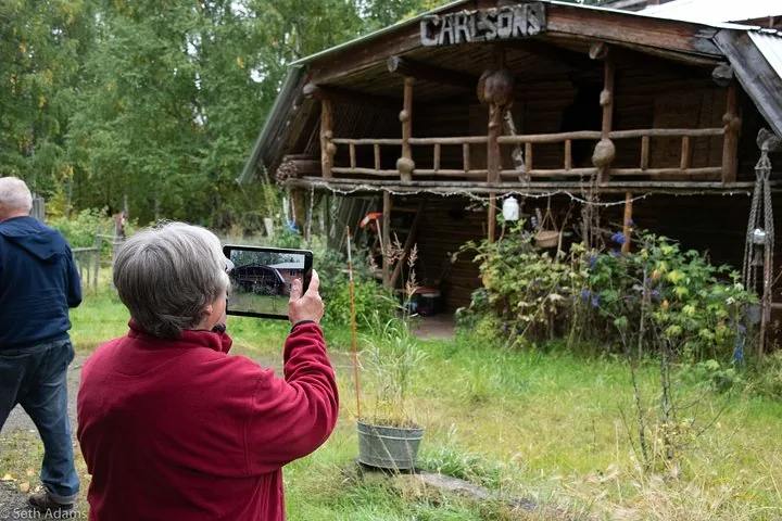 Guest photographing the old Carlsons log cabin at the Joy homestead with a tablet