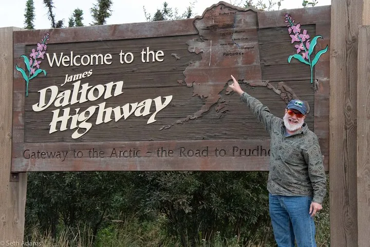 Guest pointing at the Fairbanks marker on the Welcome to the James Dalton Highway sign