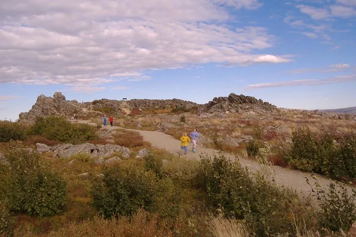 Walkers on the gravel trail among the granite tors of Finger Mountain under a wide summer sky