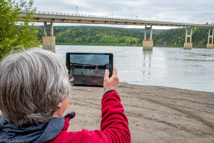 Guest photographing the Yukon River bridge from the riverbank at Yukon River Camp