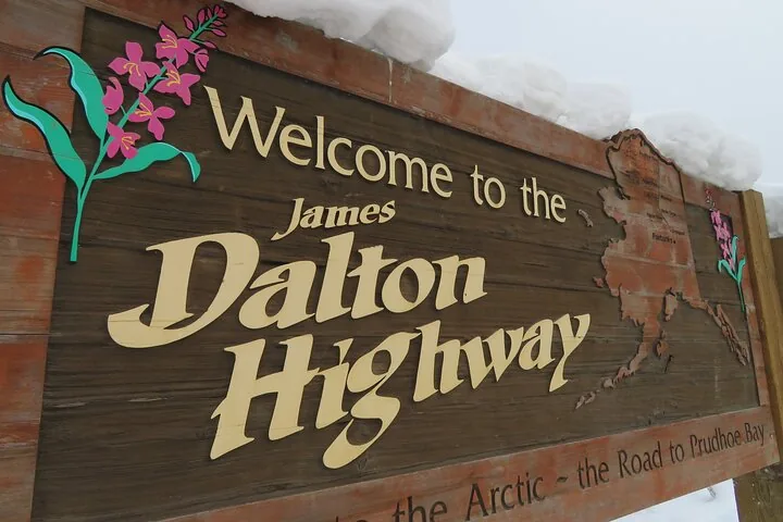 Close-up of the carved James Dalton Highway sign with snow piled along its top edge