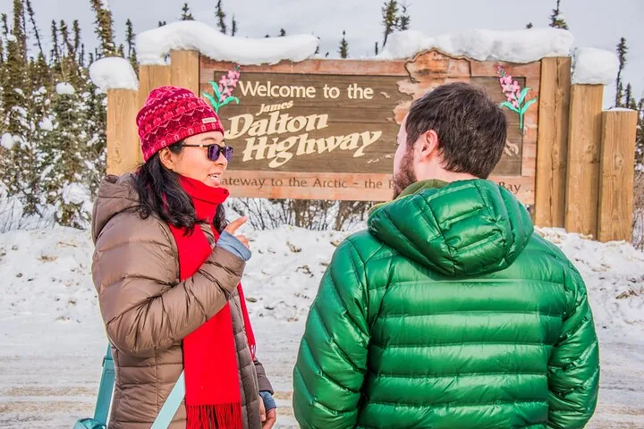 Two guests talking in front of the snow-topped Welcome to the James Dalton Highway sign