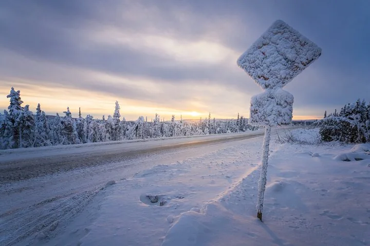 Snow-encrusted road sign beside the plowed highway at winter sunset
