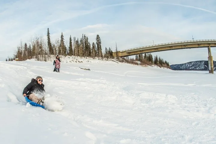 Guests sledding on the snow-covered bank below the Yukon River bridge