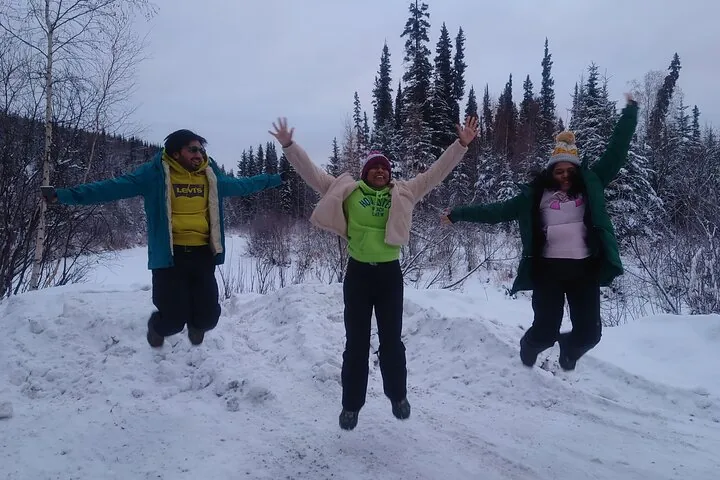 Three guests jumping for a photo on a snowy pullout with spruce forest behind