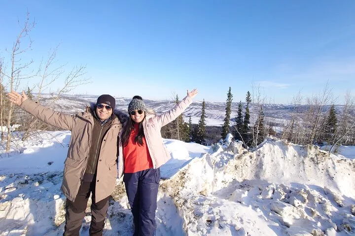 Couple with arms raised at a snowy hilltop viewpoint over the forested valleys north of Fairbanks