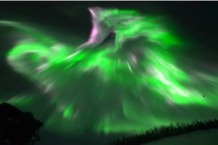 Bright green and pink aurora corona overhead, photographed from beside the van on a winter night