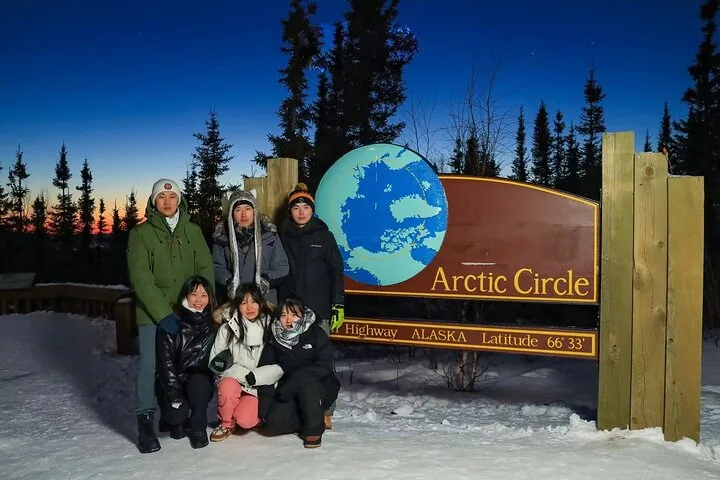 Group of six guests posing at the Arctic Circle sign at dusk