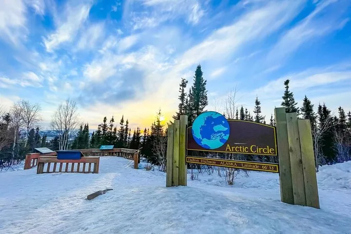 Arctic Circle sign and the wayside's picnic area and interpretive panels under a winter sunrise