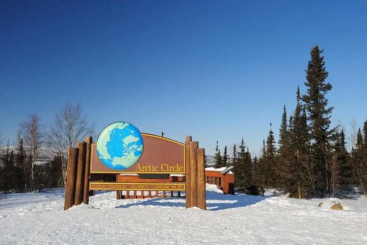 Arctic Circle sign at the Dalton Highway wayside under a clear blue winter sky