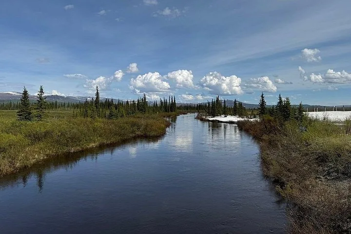Creek winding through open tundra beside the Dalton Highway with pipeline supports at the right